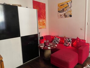 A red sofa with patterned cushions, a round table with a mushroom top, and a black and white cabinet. - Bed room in a cosy appartement Eiffel Tower (Paris)