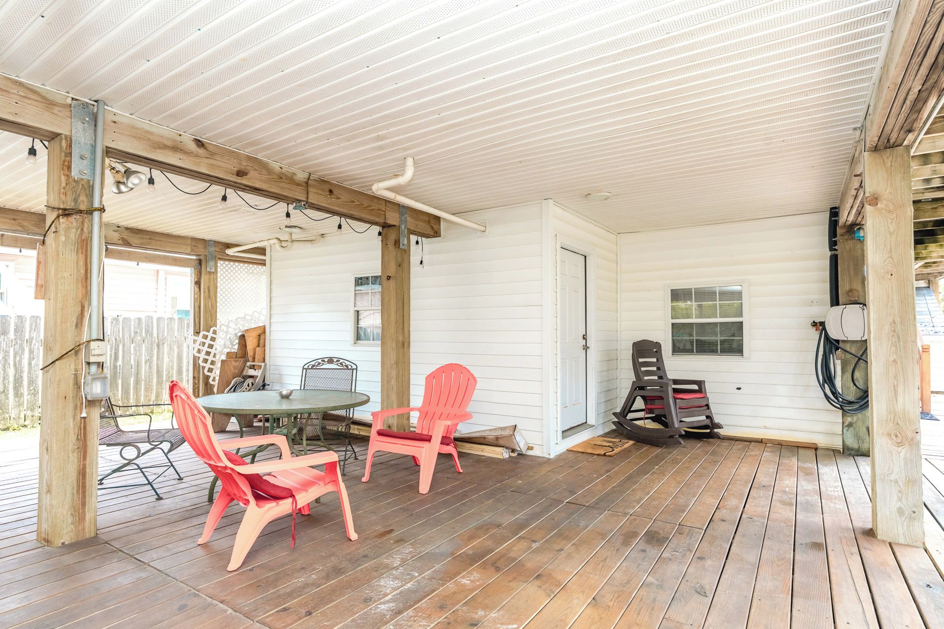A covered outdoor area with a wooden deck, a round table, and several chairs.