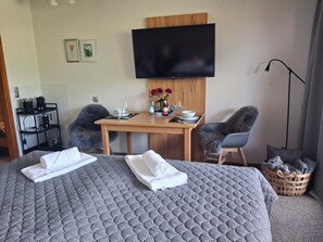 Ein Hotelzimmer mit einem Bett, einem Schreibtisch, zwei Stühlen, einem Fernseher und einer Kaffeemaschine.