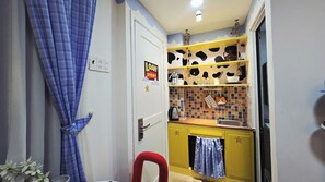 Cocina compacta con un armario amarillo, una silla roja y una cortina azul.