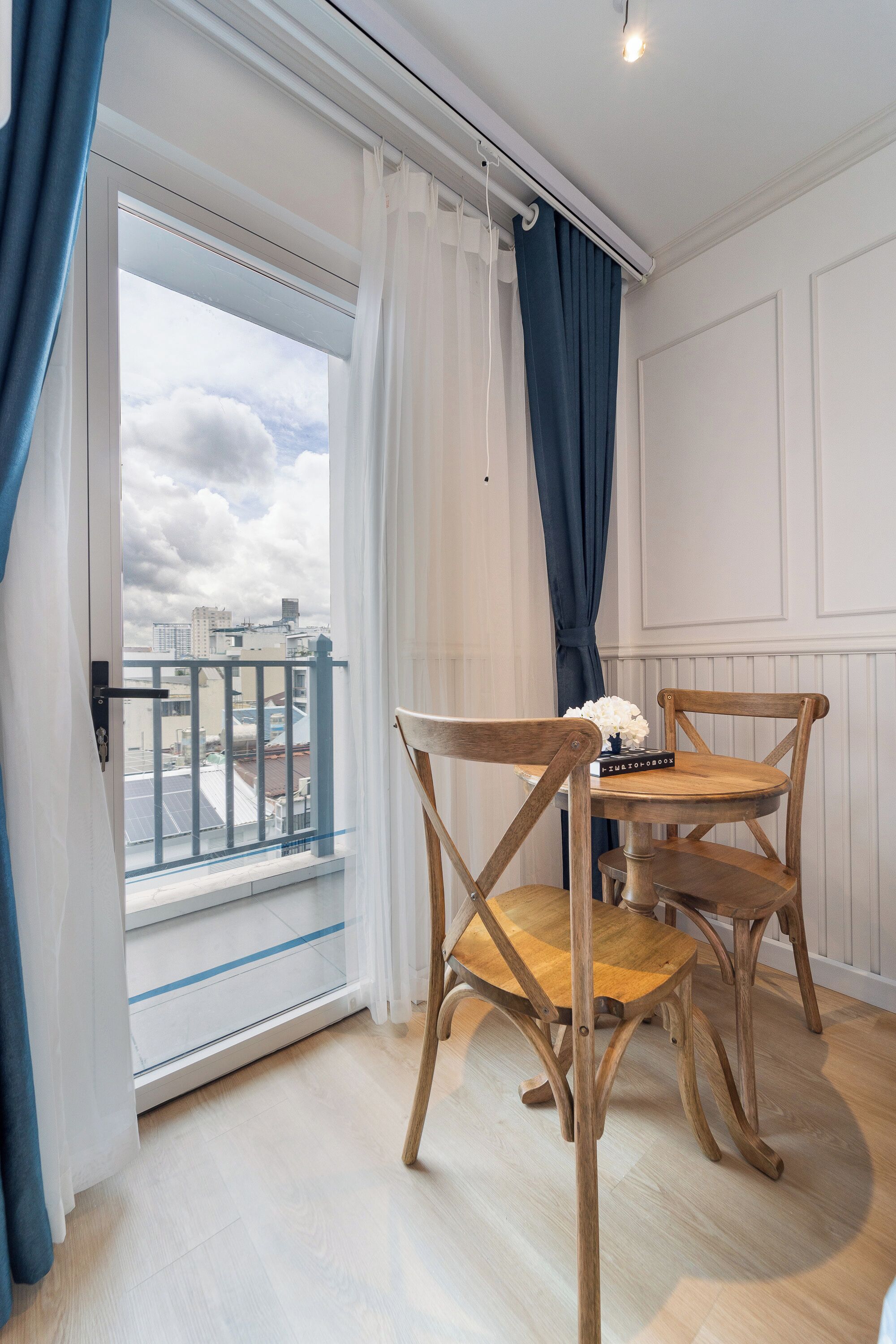 A room with a balcony, a table with chairs, and a view of the cityscape.