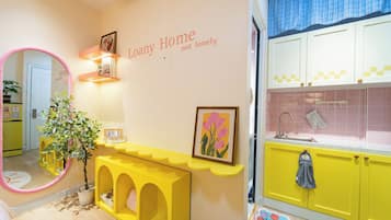 A brightly colored interior with a yellow console table, a mirror, and a wall-mounted shelf with books and a calendar.