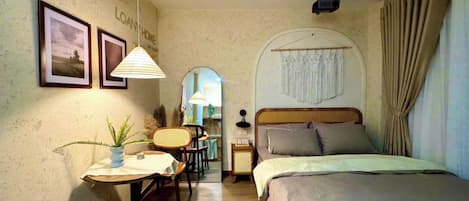 A hotel room with a bed, a desk, a chair, a lamp, a mirror, and a window with curtains.