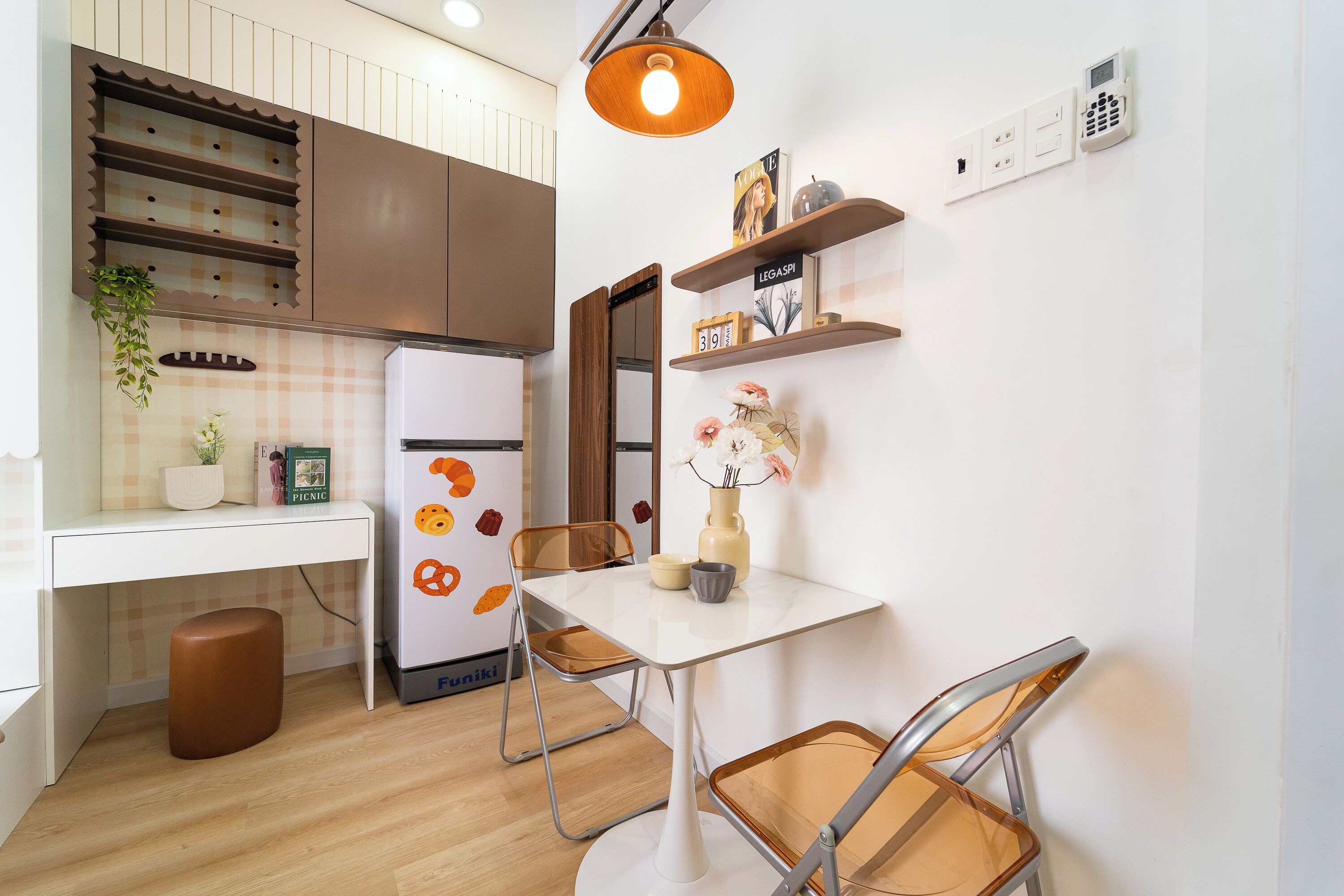 A compact kitchen with a refrigerator, a dining table, chairs, and a hanging light fixture.