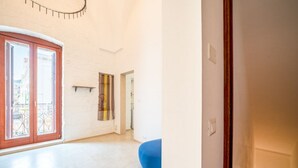 Um quarto espaçoso com uma grande porta de vidro deslizante que dá para uma varanda externa, uma poltrona de tecido azul em formato de saco e uma prateleira fixada na parede.