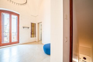 Ein geräumiges Zimmer mit einer großen Glasschiebetür, die auf einen Balkon im Freien führt, einem blauen Sitzsack und einem an der Wand befestigten Regal.