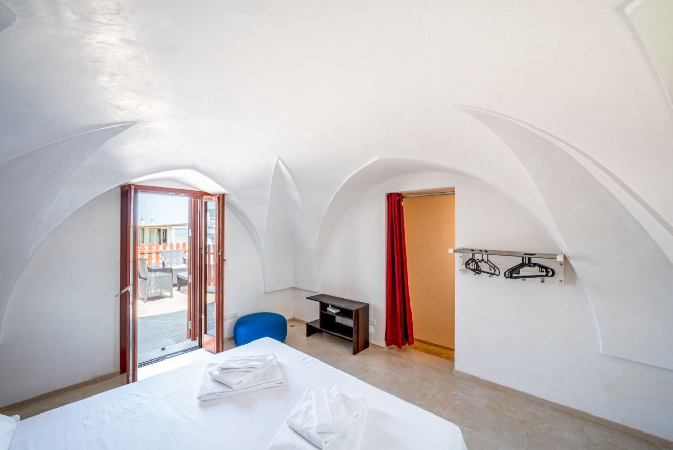 A room with a bed, a desk, and a chair. There is a door leading to an outdoor area with orange barriers.
