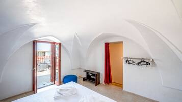 A room with a bed, a desk, and a chair. There is a door leading to an outdoor area with orange barriers.