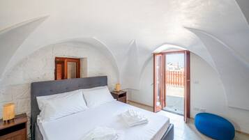 A bedroom with a bed, a nightstand, a lamp, a blue chair, and a view through an open door.