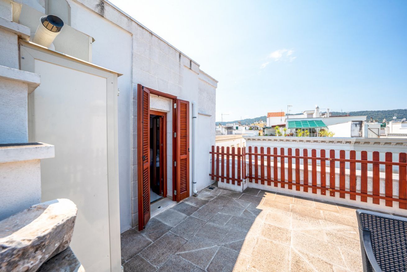A balcony with a red wooden fence, a stone floor, and a white building with a door.