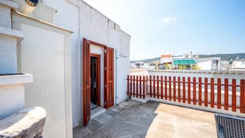 A balcony with a red wooden fence, a stone floor, and a white building with a door.