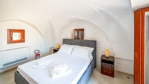 Quarto com uma cama, uma mesa de cabeceira, radiador fixado na parede e extintor de incêndio.