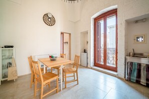 Ein Essbereich mit Holztisch und Stühlen, einer dekorativen Wanduhr sowie eine Küchenzeile mit Fenster und Balkon.