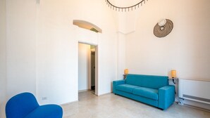 Uma sala de estar moderna com um sofá e uma poltrona azuis, uma parede branca com um desenho circular e uma porta que dá para outro cômodo.