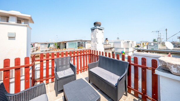 Terraço no terraço com mobiliário de vime e guarda-corpo vermelho.