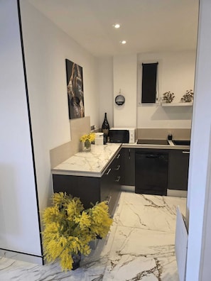 Eine moderne Küche mit Marmorarbeitsplatte, schwarzen Schränken und einer kleinen Kochinsel mit einer Vase voller gelber Blumen.