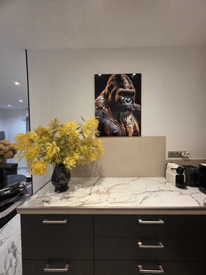 Eine moderne Küche mit Marmorarbeitsplatte, einem Blumenstrauß aus gelben Blumen, einem großen Gorilla-Poster und dunklen Schränken.