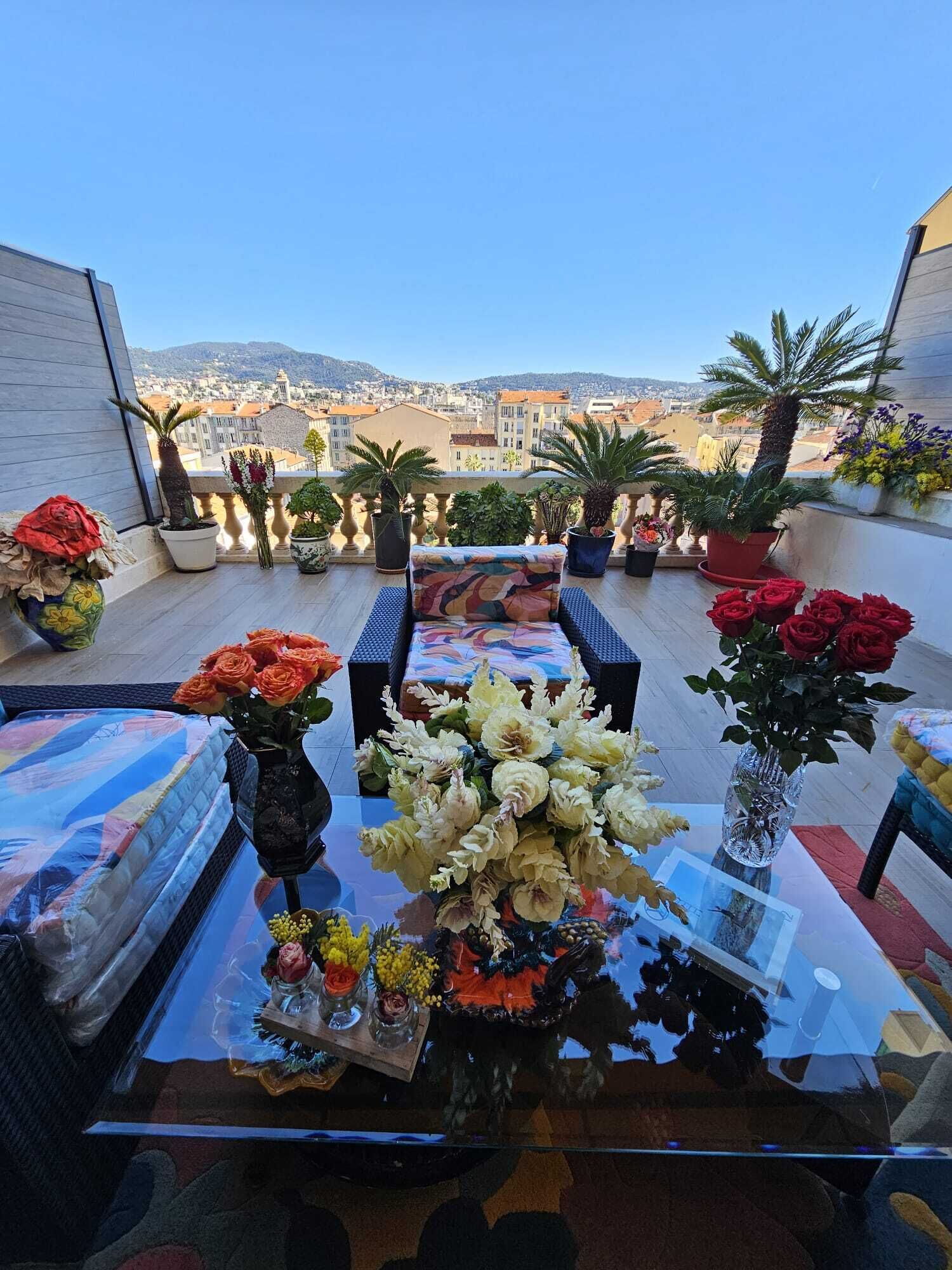 A rooftop terrace with a table set for dining, surrounded by potted plants and flowers.