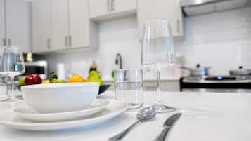 Uma cozinha moderna com armários brancos, bancada de mármore, uma tigela de frutas e uma taça de vinho.