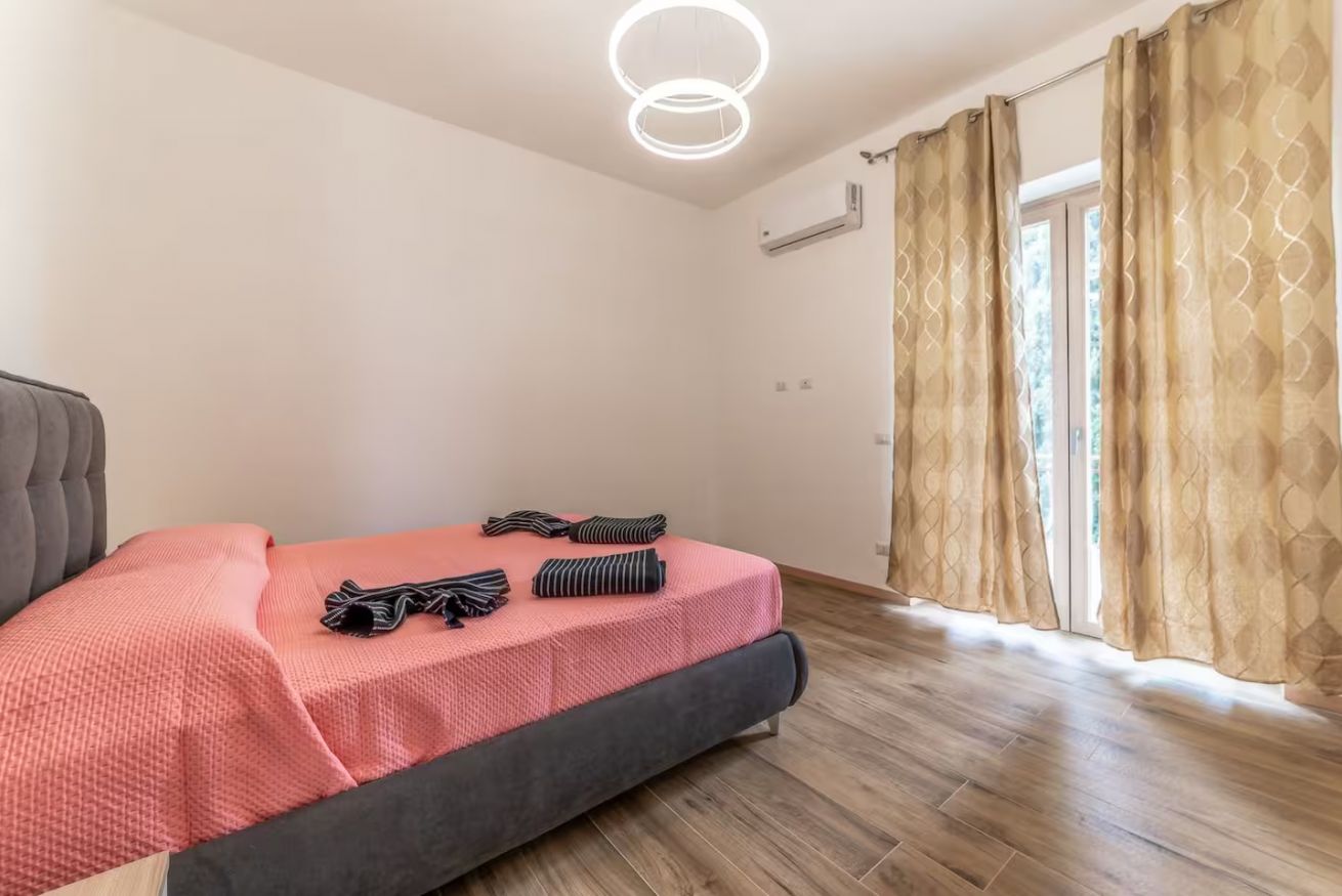 Una camera da letto con un letto, una testiera grigia, una lampada a sospensione e una finestra con tende.