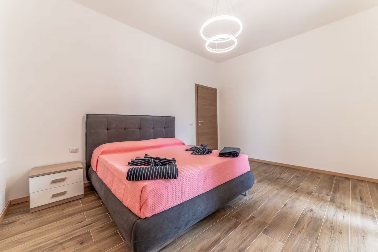A bedroom with a bed, a nightstand, a door, and a modern light fixture.