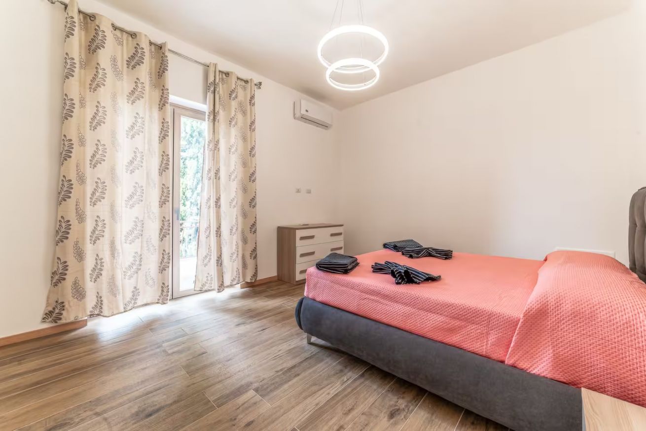 Een slaapkamer met een bed, een dressoir, een plafondlamp en een raam met gordijnen.