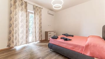 Een slaapkamer met een bed, een dressoir, een plafondlamp en een raam met gordijnen.