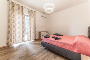 Une chambre à coucher avec un lit, une commode, un luminaire au plafond et une fenêtre avec des rideaux.