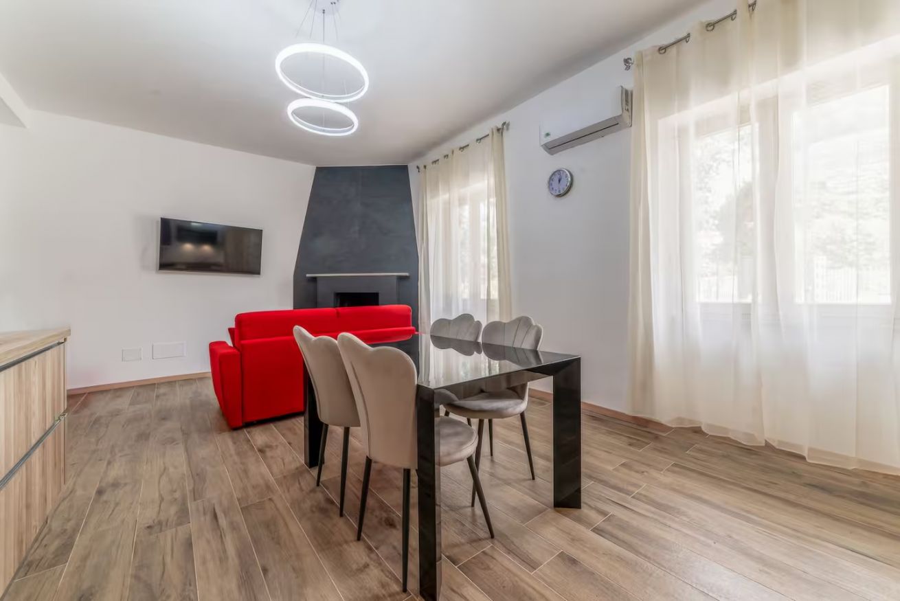 Ein modernes Wohnzimmer mit Essbereich, einem roten Sofa, einem Kamin und einem an der Wand befestigten Flachbildfernseher.