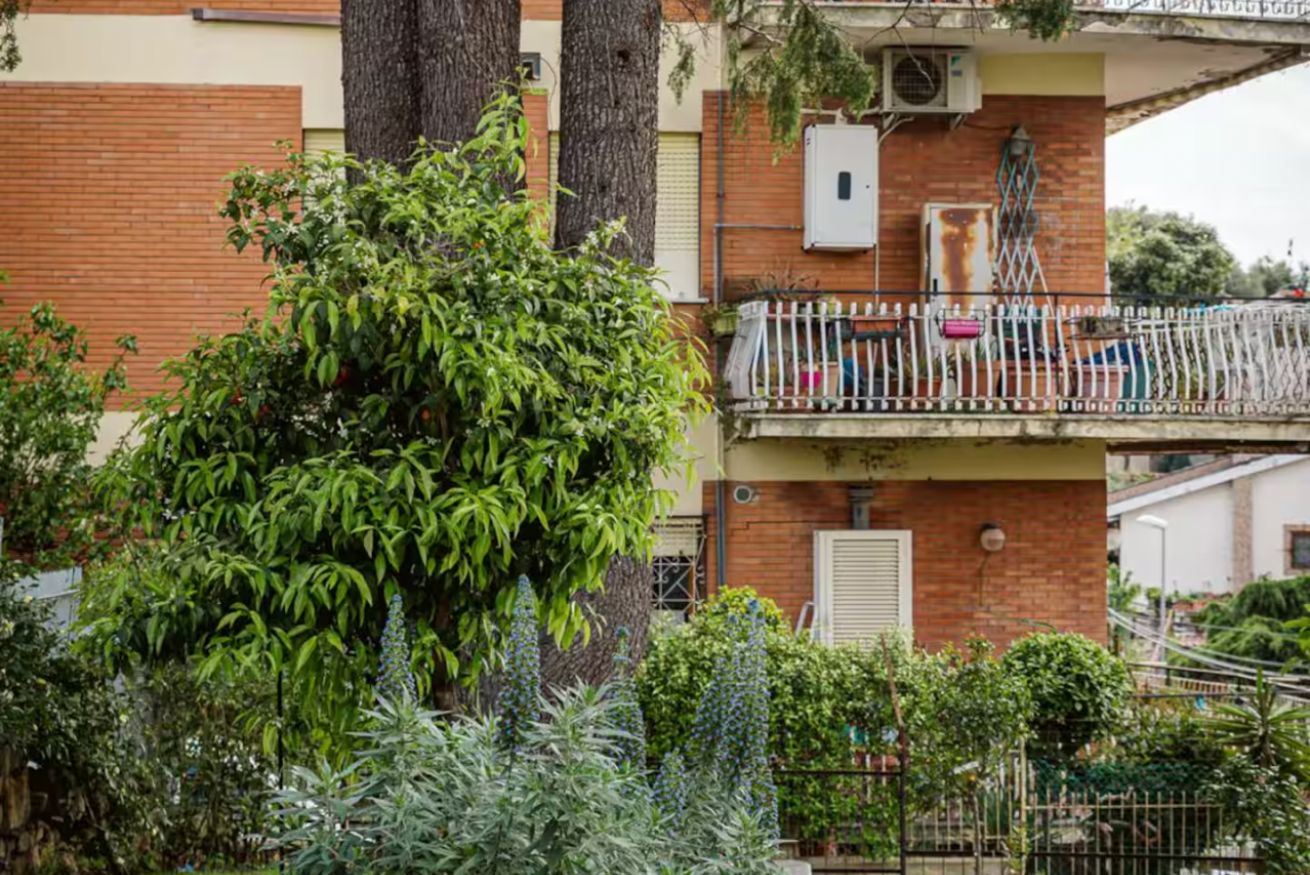 Un immeuble résidentiel doté d’un balcon, avec un arbre au premier plan et un mur de briques.