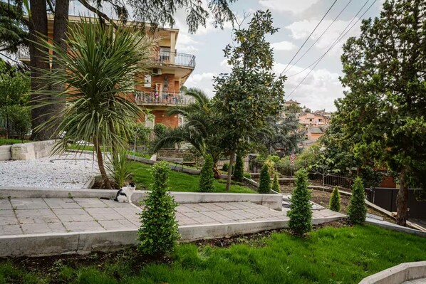 Un quartier résidentiel comprenant un immeuble à plusieurs étages, une cour pavée et une variété d’arbres et d’arbustes.