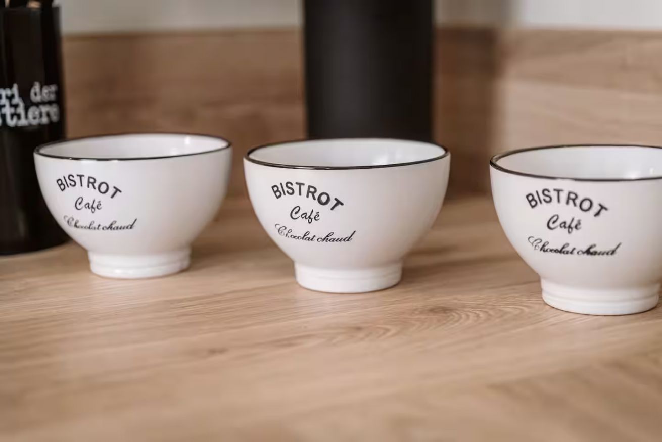Drie witte keramieken kommen met zwart tekst op een houten ondergrond.