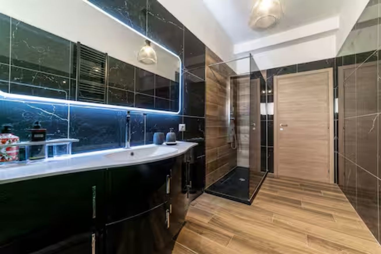 Une salle de bain moderne avec un grand miroir, une douche et un meuble-lavabo avec un évier.