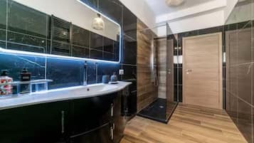 A modern bathroom with a large mirror, a shower, and a vanity with a sink.