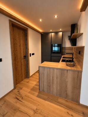 Une cuisine moderne avec un îlot central en bois, des appareils électroménagers intégrés et une porte en bois.