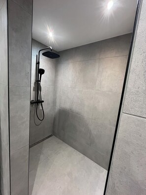 Une douche moderne dotée d’un pommeau de douche à main et d’un panneau de commande fixé au mur.