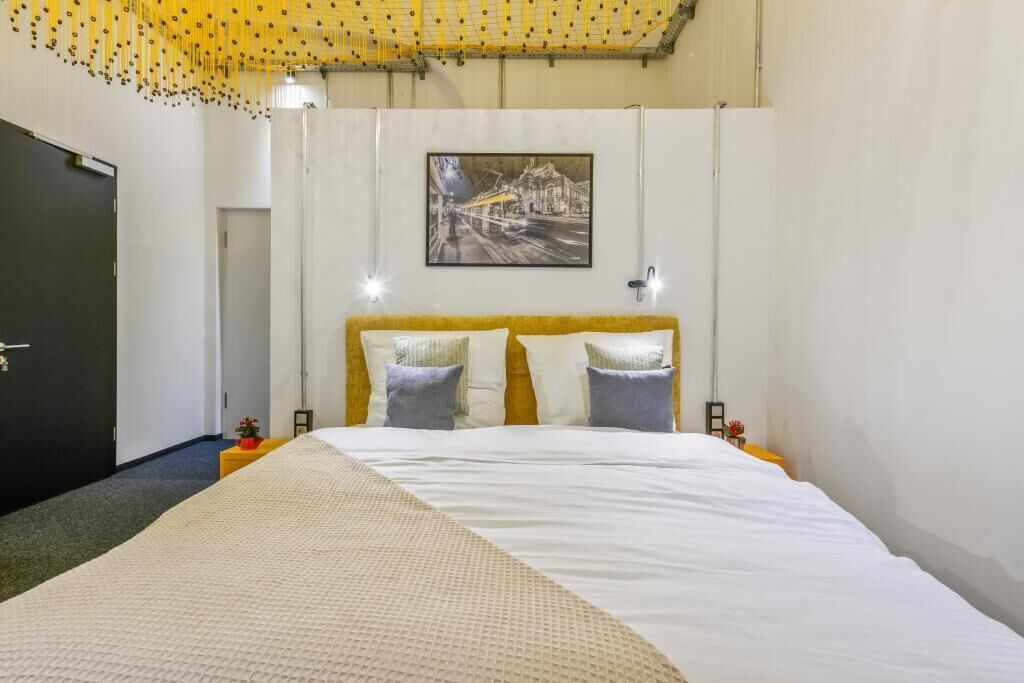 Habitación de hotel con una cama grande, un cuadro en la pared y una puerta a la izquierda.