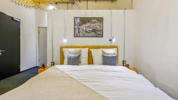 Habitación de hotel con una cama grande, un cuadro en la pared y una puerta a la izquierda.