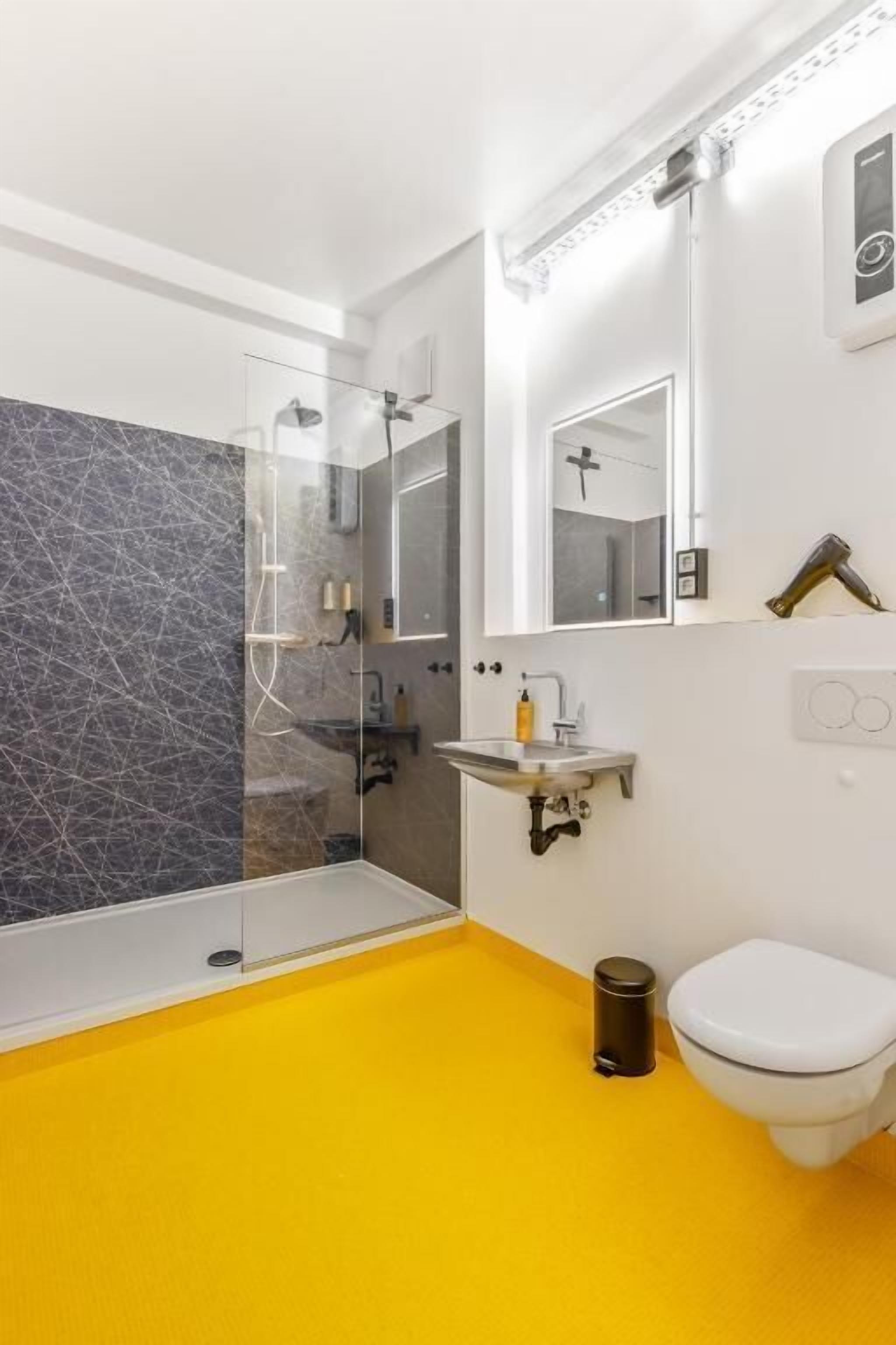 Ein Badezimmer mit Duschkabine aus Glas, Waschbecken in Weiß und einem Spiegel sowie einer Toilette.