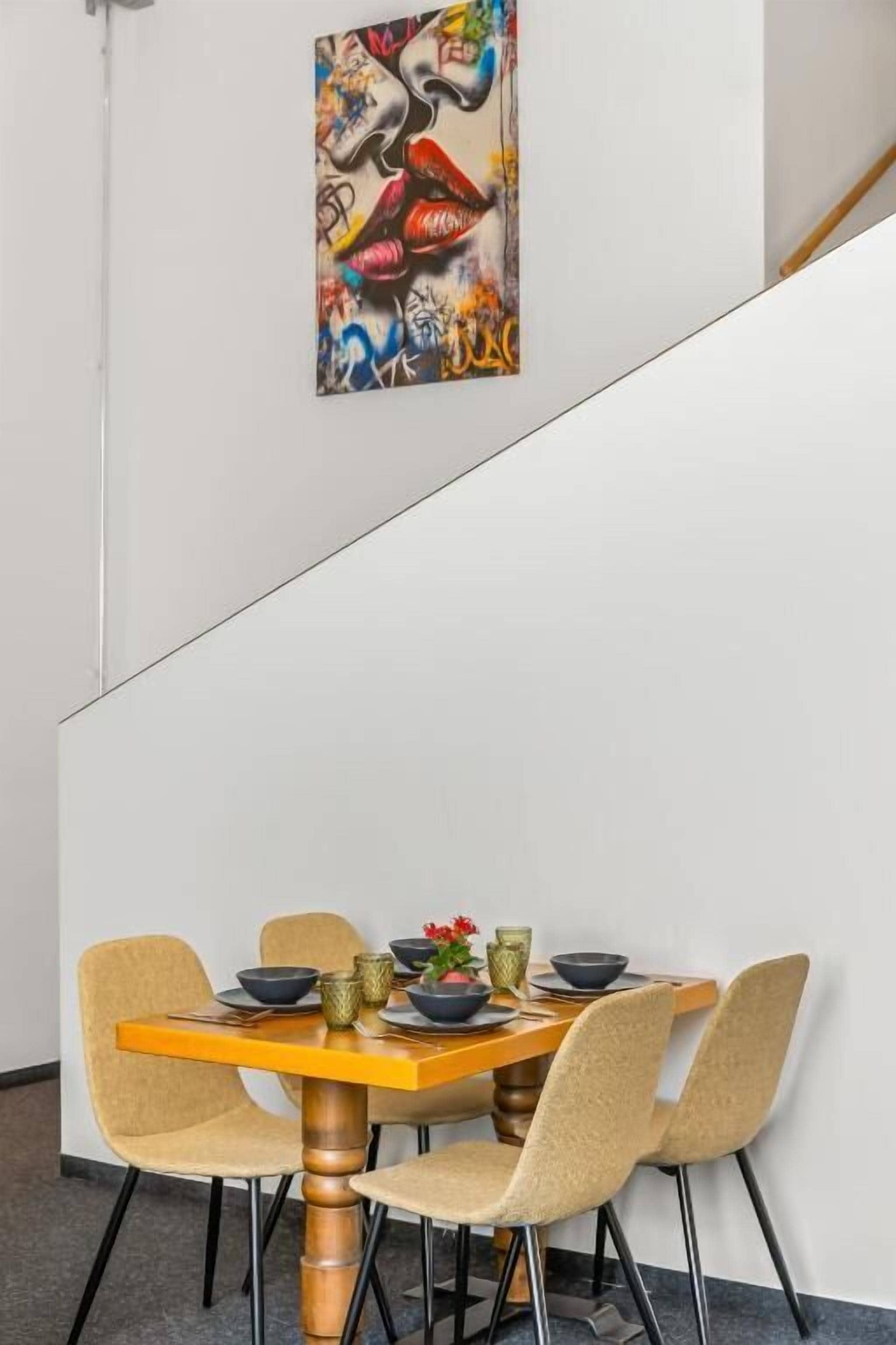 Ein Essbereich mit einem Tisch für vier Personen, Stühlen und einem farbenfrohen, abstrakten Gemälde an der Wand.