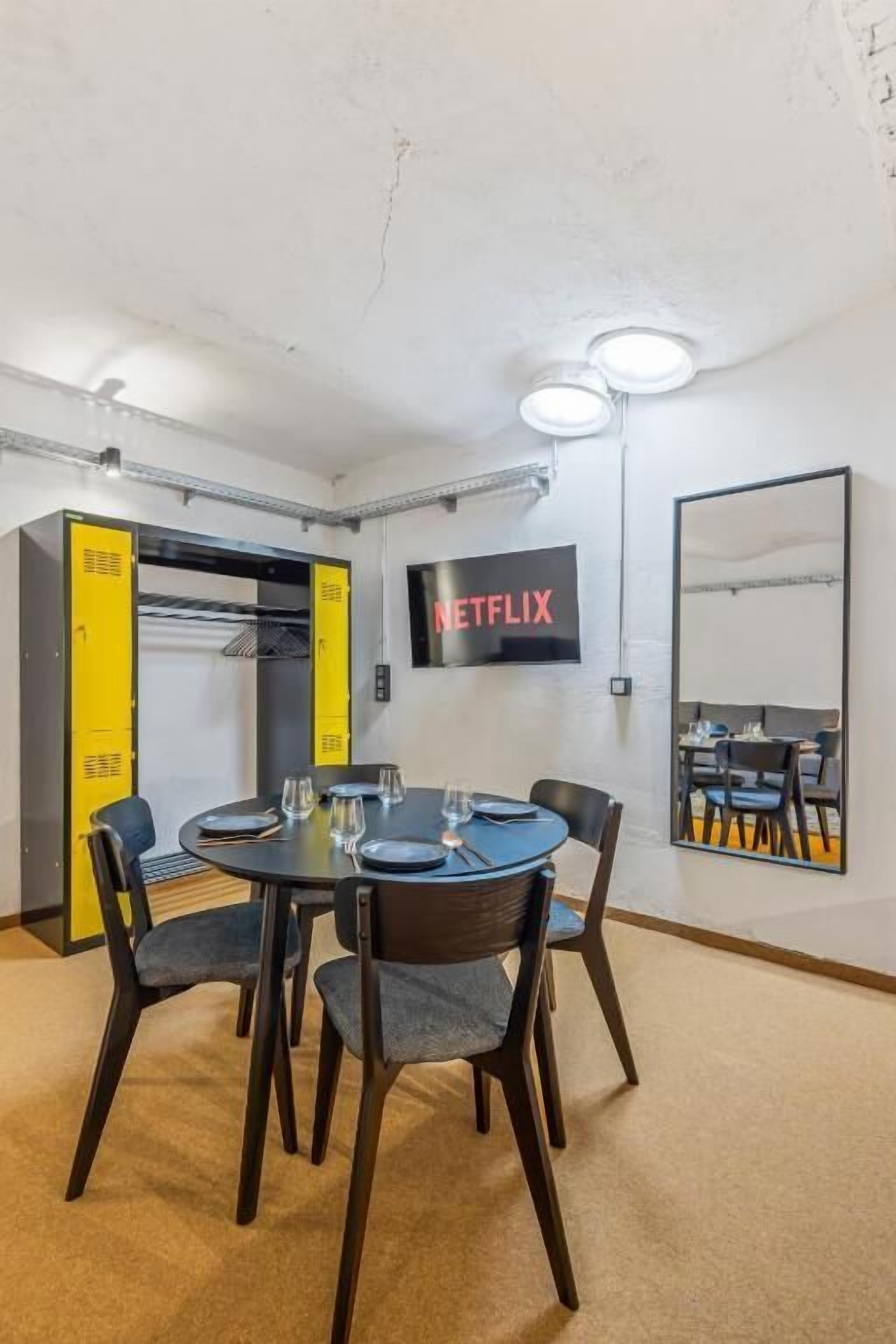 A room with a round table, chairs, a television, and a yellow cabinet.