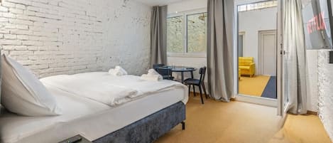 A hotel room with a large bed, a desk, a chair, a TV, and a view through the window.
