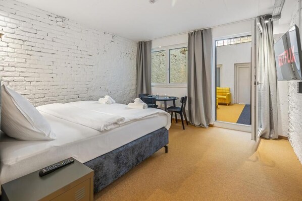 A hotel room with a large bed, a desk, a chair, a TV, and a view through the window.