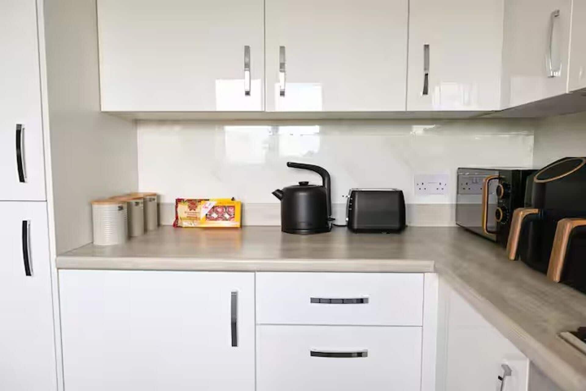 Una cocina con armarios blancos, hervidor, tostadora y cafetera.