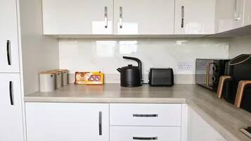 Una cocina con armarios blancos, hervidor, tostadora y cafetera.