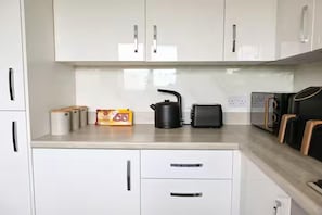 A kitchen with white cabinets, a kettle, a toaster, and a coffee machine.