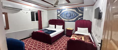 A room with a bed, a small table, a ceiling fan, and a wall-mounted TV.
