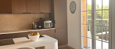 A kitchen with a wooden ceiling, a large window, and a bar area with a bowl of fruit.