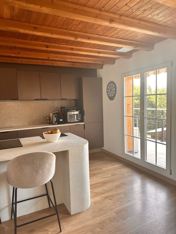 A kitchen with a wooden ceiling, a large window, and a bar area with a bowl of fruit.