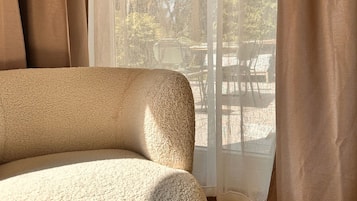 Ein Zimmer mit einer Couch, einem Fenster mit leichtem Vorhang und Blick auf einen Außenbereich.